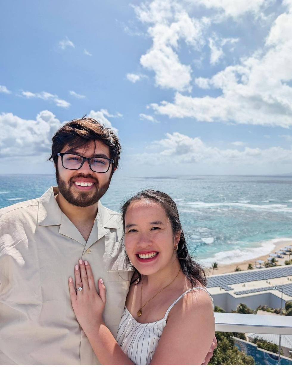 Jocelyn and Devanshu smiling by the ocean just after their engagement, Jocelyn showing her ring